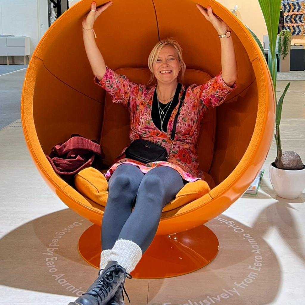 Iloisesti hymyilevä Henna Karhunen istuu oranssissa pallotuolissa.